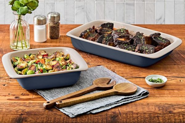 Two rectangular baking dishes containing cooked food on a wooden table with kitchen items in the background Credit: Amazon