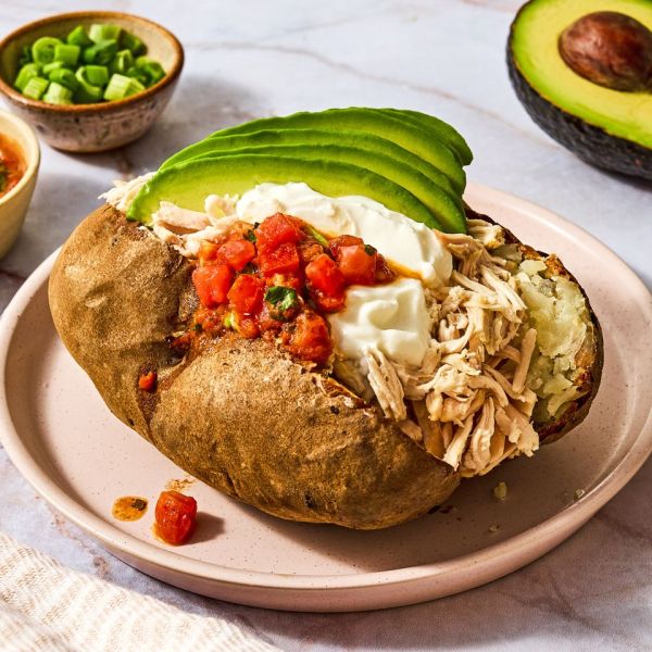 A stuffed baked potato topped with shredded chicken diced tomatoes sour cream and avocado slices with garnish bowls in the background Credit: Ali Redmond