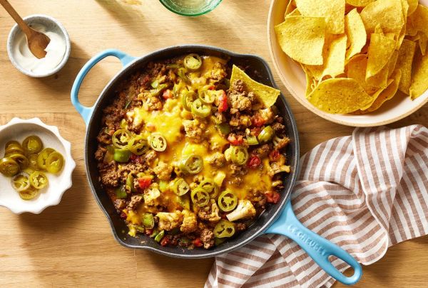 Cheesy ground beef & cauliflower casserole recipe with one tortilla chip scooping casserole out, a bowl of more chips is on the side of the casserole skillet Credit: Photographer: Brie Goldman, Food Stylist: Holly Dreesman, Prop Stylist: Gabriel Greco