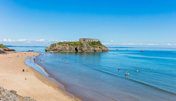 View of Tenby coastline with St Catherine's Island as the focal point. The sky and sea is blue and inviting. You can see people 