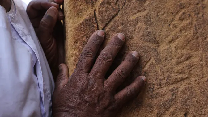 Seorang pengunjung menyusurkan tangannya pada blok-blok batu sebuah piramida di situs arkeologi Meroe di Bejrawiya, Sudan, Minggu, 2 Agustus 2026. (Foto AP/Mohnd Blal)