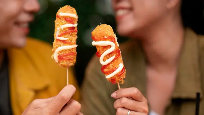 Dua orang sedang menunjukkan kuliner kekinian corndog sosis (Sumber: Freepik)