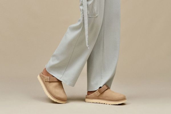 A person wearing lightcolored pants and a pair of beige clogs with a strap walking on a neutral background Credit: Nordstrom Rack
