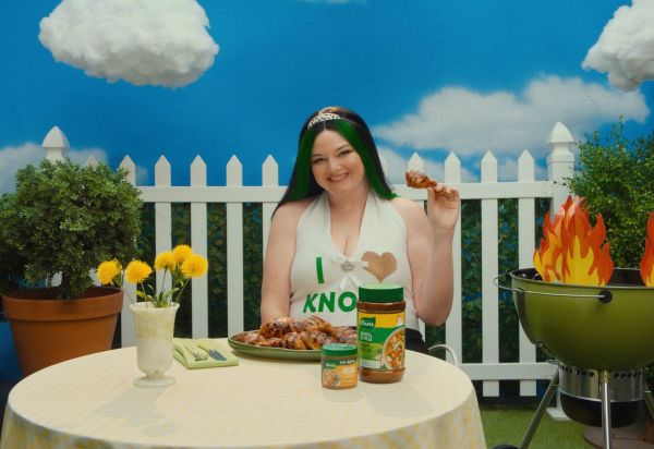 A person sitting at a table with cooked food in an outdoor setting holding a rib Credit: Courtesy of Knorr