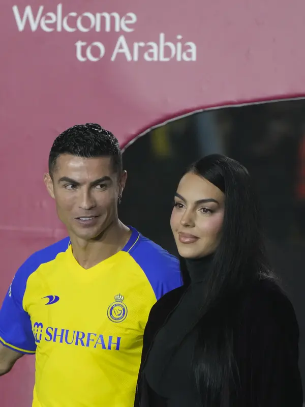 Cristiano Ronaldo menatap sang kekasih Georgina Rodriguez saat mereka menghadiri upacara penyambutan dirinya sebagai pemain baru Al Nassr di Stadion Mrsool Park, di ibu kota Saudi, Riyadh, Selasa (3/1/2023). Kekasih CR7 yang biasanya kerap memamerkan kemolekan tubuhnya terlihat lebih sopan dalam berpakaian. (AP Photo/Amr Nabil)