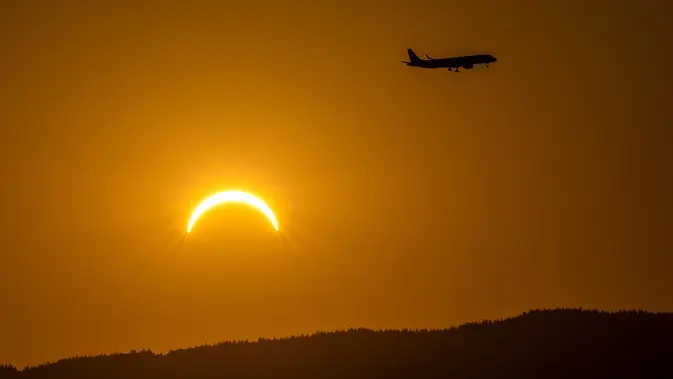 Sebuah pesawat terbang melintas saat gerhana matahari sebagian di Bernex dekat Jenewa, Swiss, Rabu, 12 Agustus 2026. (Martial Trezzini/Keystone via AP)