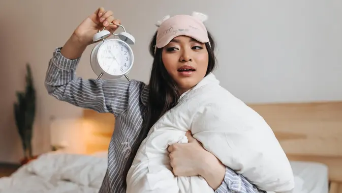 ilustrasi perempuan di tempat tidur sambil memegang jam weker/copyright freepik.com/lookstudio