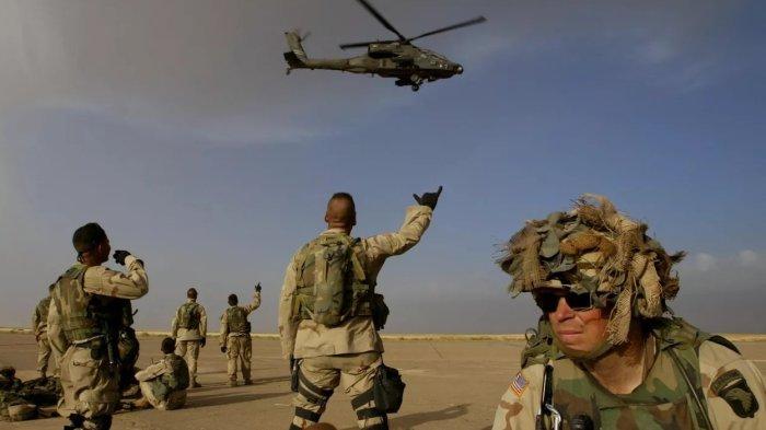 Tentara dari Batalyon ke-3 Brigade Lintas Udara 101 berkumpul di landasan udara menunggu helikopter menjemput mereka untuk menjalankan misi, beberapa melambai ke helikopter serbu Apache yang lewat, di sebuah pangkalan di barat laut Irak, sekitar 100 kilometer dari perbatasan Suriah, Minggu, 18 Mei 2003 -