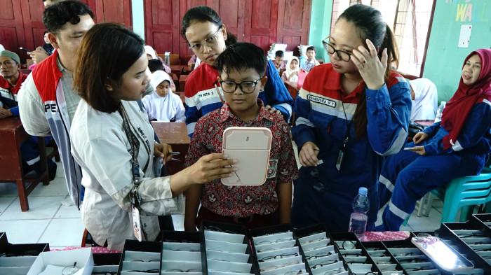Perwira Pertamina EP Pangkalan Susu mendampingi siswa dalam kegiatan pemeriksaan mata gratis melalui program Lensa Energi.