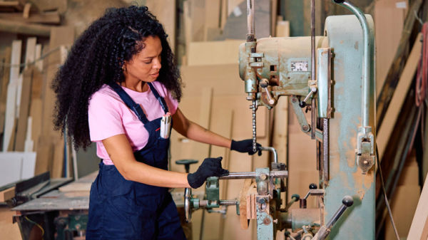 Young woman operating a heavy-duty drill press in an industrial carpentry workshop