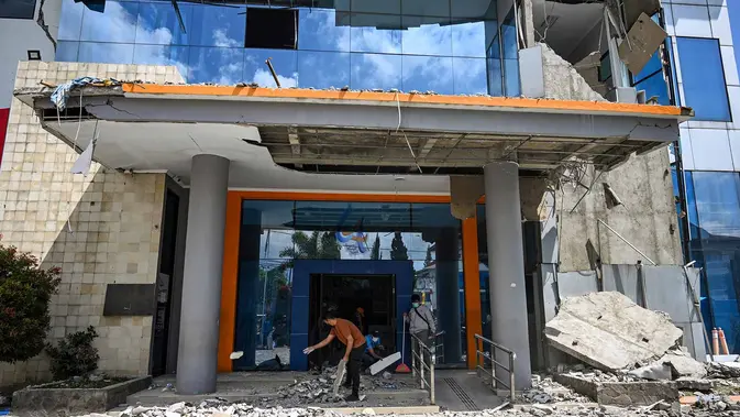 Pekerja membersihkan puing-puing dari sebuah gedung bank yang rusak akibat gempa berkekuatan magnitudo 7,7 di Ruteng, Manggarai, Nusa Tenggara Timur, Minggu, 16 Agustus 2026. (AFP/ Juni Kriswanto)