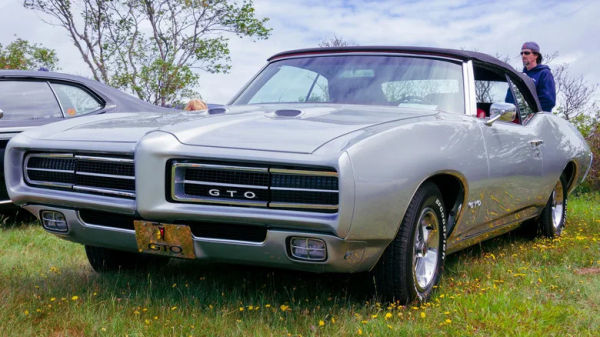 A rare gray 1969 Pontiac GTO without Judge decals, parked on the grass at a car show.