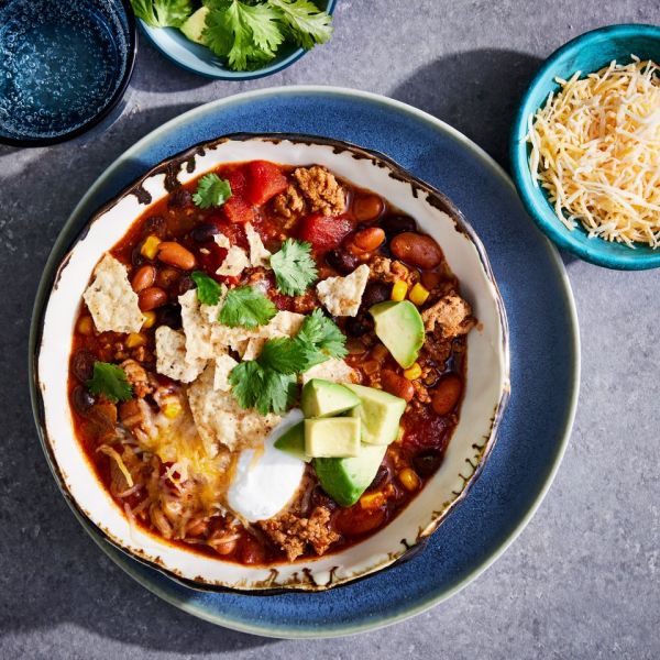 a recipe photo of the Everyone's Favorite Taco Soup served in a bowl and topped with cilantro, avocado, tortilla chips, sour cream, and cheese Credit: Photographer: Jen Causey, Prop Stylist: Claire Spollen, Food Stylist: Ali Ramee