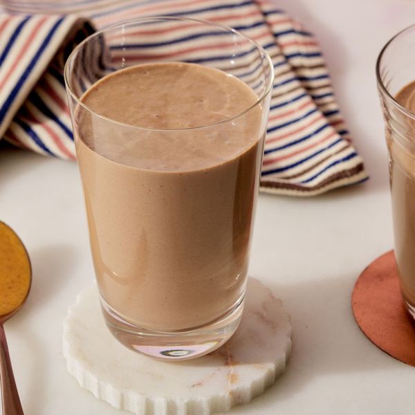 side shot of a light brown smoothie in a tall glass with a striped napkin behind Credit: Photographer: Fred Hardy, Food Stylist: Margaret Monroe Dickey