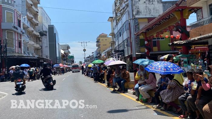 Sejumlah warga menggunakan payung untuk berlindung dari terik matahari saat menyaksikan pawai baris-berbaris (PBB) di Jalan Ahmad Yani, Kota Pangkalpinang, Rabu (26/8/2026). Meski cuaca panas, antusiasme masyarakat menyaksikan kemeriahan pawai tetap tinggi.