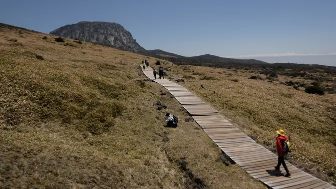 Pejalan kaki berjalan di depan puncak Hallasan, atau gunung Halla, di pulau Jeju, Korea Selatan (9/5/2019). Pulau Jeju adalah satu-satunya provinsi berotonomi khusus Korea Selatan. (AFP Photo/Ed Jones)