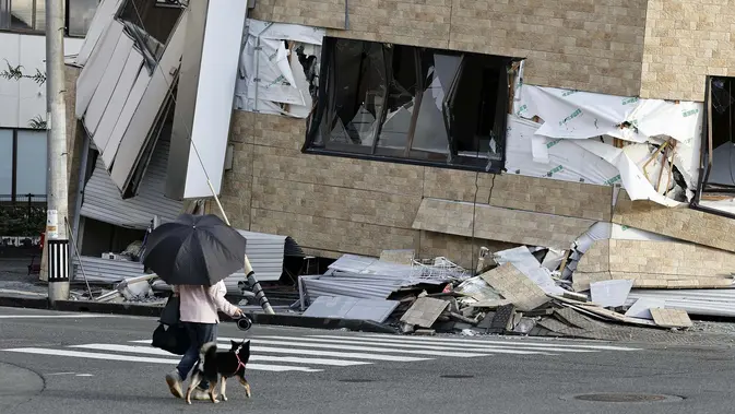 Warga berjalan bersama anjingnya melewati bangunan yang runtuh akibat gempa bumi di Yatsushiro, prefektur Kumamoto, Rabu, 29 Juli 2026. (Juntaro Yokoyama/Kyodo News via AP)