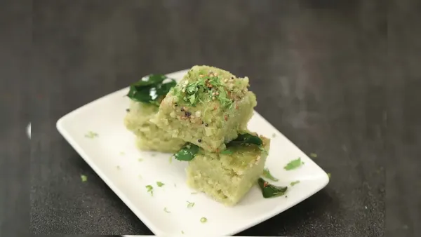Spongy green moong dal dhokla cubes tempered with mustard seeds and curry leaves served on white plate.