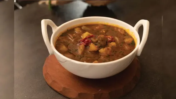 Delicious spicy Indian aloo mamatar curry garnished with red chili in ceramic bowl on wooden base.