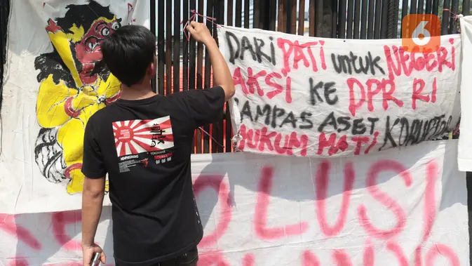 Seorang pengunjuk rasa memasang spanduk berisi tuntutan di pagar gedung DPR saat mengikuti aksi Aliansi Masyarakat Pati Bersatu (AMPB) di Jakarta, Kamis (27/8/2026). (KLY/Budy Santoso)