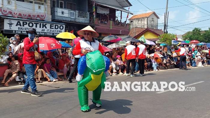 HIBUR MASYARAKAT -- Bupati Bangka Selatan, Riza Herdavid ketika menghibur masyarakat menggunakan kostum dinosaurus saat pawai dan karnaval HUT RI, Kamis (27/8/2026). Aksi tersebut dilakukan dalam rangka penggalangan dana untuk masyarakat NTT.