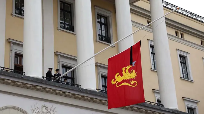 Bendera kerajaan yang dihiasi pita hitam dikibarkan setengah tiang oleh anggota Pasukan Pengawal Kerajaan dari balkon istana setelah Raja Harald V dari Norwegia wafat di Oslo, Norwegia, Jumat, 28 Agustus 2026. (AFP/ Odd Andersen)