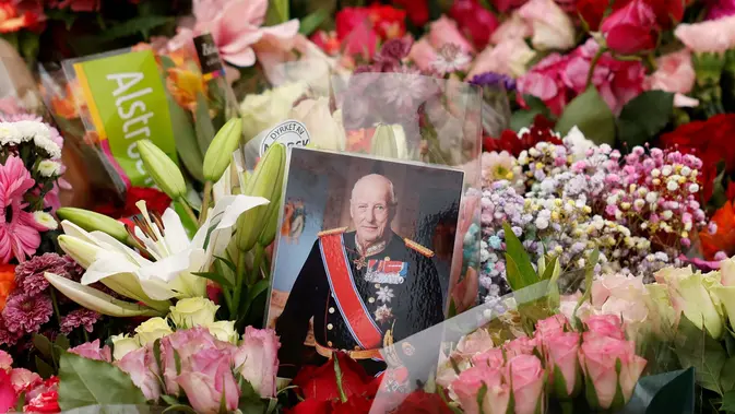 Sebuah foto kecil Raja Harald V dari Norwegia terlihat di antara bunga-bunga di lokasi penghormatan sementara di alun-alun Istana Kerajaan di Oslo, Norwegia, Jumat, 28 Agustus 2026. (AFP/ Odd Andersen)