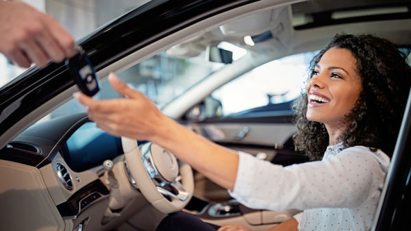 A woman in the driver's seat of a car with the door open being handed the key