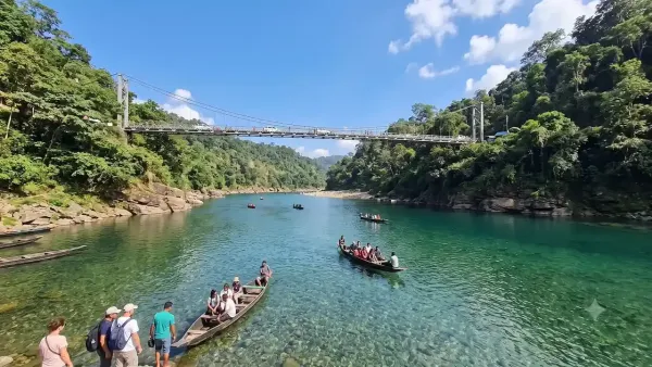 Tourists enjoying wooden boat rides on crystal clear emerald waters of Umngot river under Dawki suspension bridge.