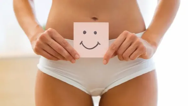 Woman holding a paper with a happy smiley face on her lower abdomen representing digestive and gut health.