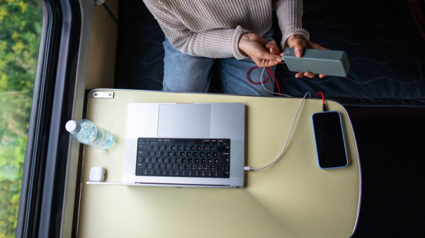 Person powering their laptop and phone from a power bank on a train