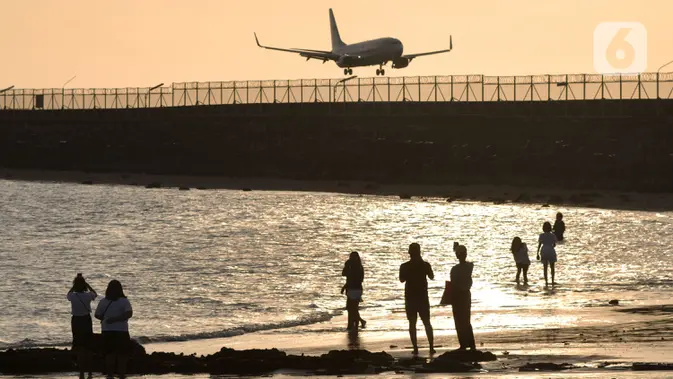 Wisatawan mengunjungi objek wisata Pantai Kelan dengan latar belakang pesawat yang mendarat di Tuban, Badung, Denpasar, Bali. (merdeka.com/Arie Basuki)