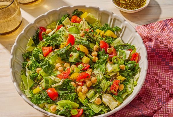 Chopped salad in a white bowl featuring lettuce tomatoes chickpeas and a vinaigrette set on a lightcolored surface with a cloth napkin
