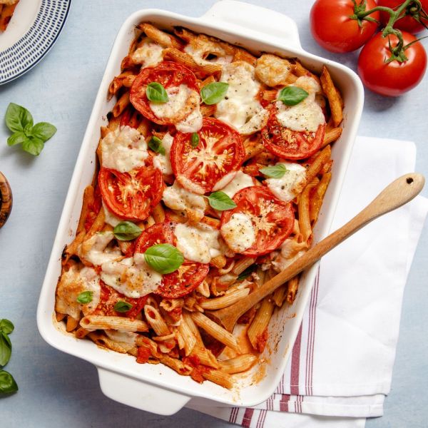 a recipe photo of the Caprese Casserole served in a dish with a wooden spoon dipped in it and tomatoes, basil, and a towel beside it Credit: Sara Haas