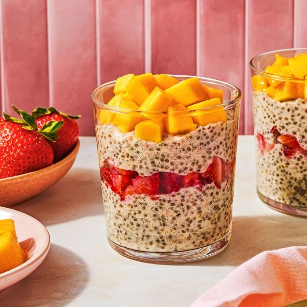 Chia pudding in a glass topped with mango and strawberries with extra fruit nearby Credit: Ali Redmond