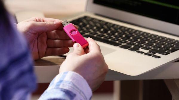 A picture of a woman holding a pink USB flash drive, sitting in front of a laptop