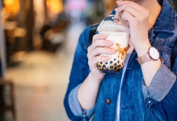 Young girl in denim jacket is drinking brown sugar flavored tapioca pearl bubble milk tea with glass straw in night market of Taiwan, close up, bokeh