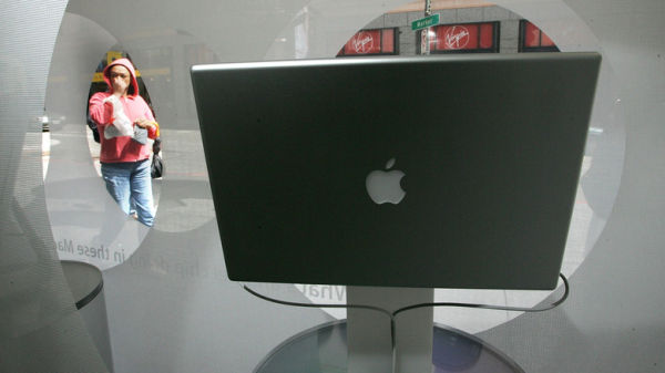 A woman looking through a window at an older Apple MacBook, showing a metallic apple logo