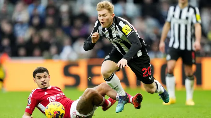 Pemain Newcastle United, Lewis Hall, terjatuh saat berebut bola dengan pemain Nottingham Forest, Morgan Gibbs-White, dalam lanjutan Liga Inggris di St James Park, Selasa (26/12/2023). (AFP/Andu Buchanan)