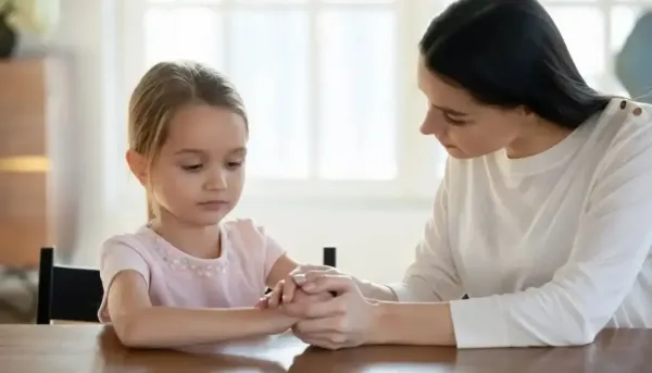 A mother gently holding her young daughter's hand while having a serious conversation, representing emotional support and discussion about a mother's remarriage.
