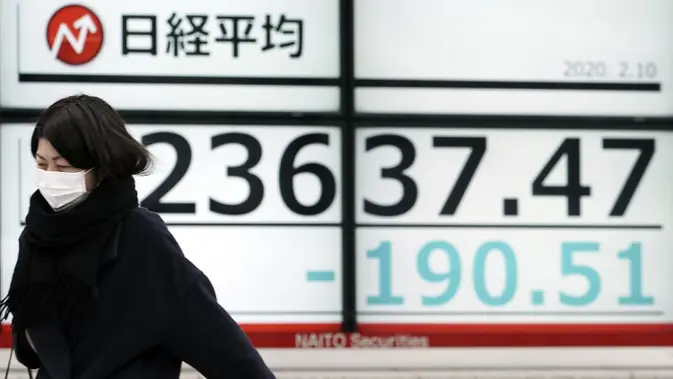 Seorang wanita berjalan melewati layar monitor yang menunjukkan indeks bursa saham Nikkei 225 Jepang dan lainnya di sebuah perusahaan sekuritas di Tokyo. (AP Photo/Eugene Hoshiko)